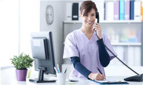 white female nurse smiling and in clinic talking to patient on phone
